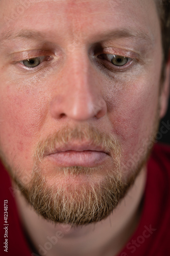 a close up portrait of a man in a red sweater and a disturbed facial expression and a desperate look