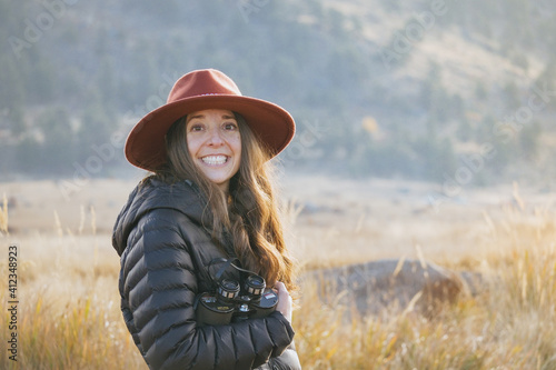 A young woman in a red felt hat enjoys nature with a pair of binoculars. 