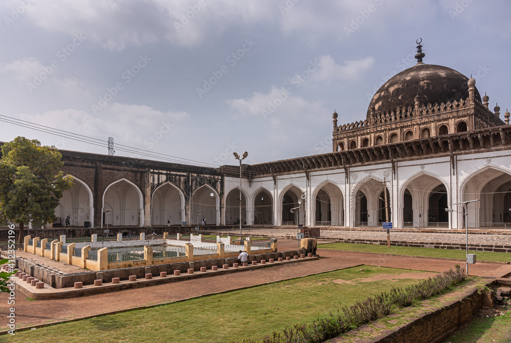 Vijayapura, Karnataka, India - November 8, 2013: Jamiya Mashid or mosque. Wide Courtyard with brown pathways among green lawn in fron tof prayer hall with blackend dome on top.