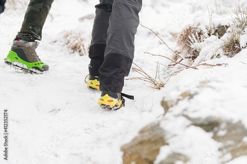 Close-up of tourists' legs and their winter boots with crampons. Snow-covered trails in the mountains.