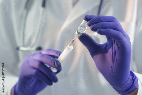 Doctor with a stethoscope in a medical gown and protective gloves is filling a syringe with a vaccine