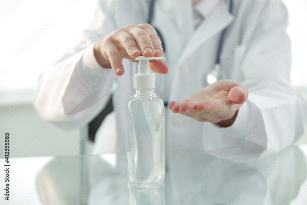 Doctor with a stethoscope in a protective mask in a clinic treats his hands with an antiseptic. Close-up Doctor with a stethoscope in a protective mask in a clinic treats his hands with an antiseptic. Close-up