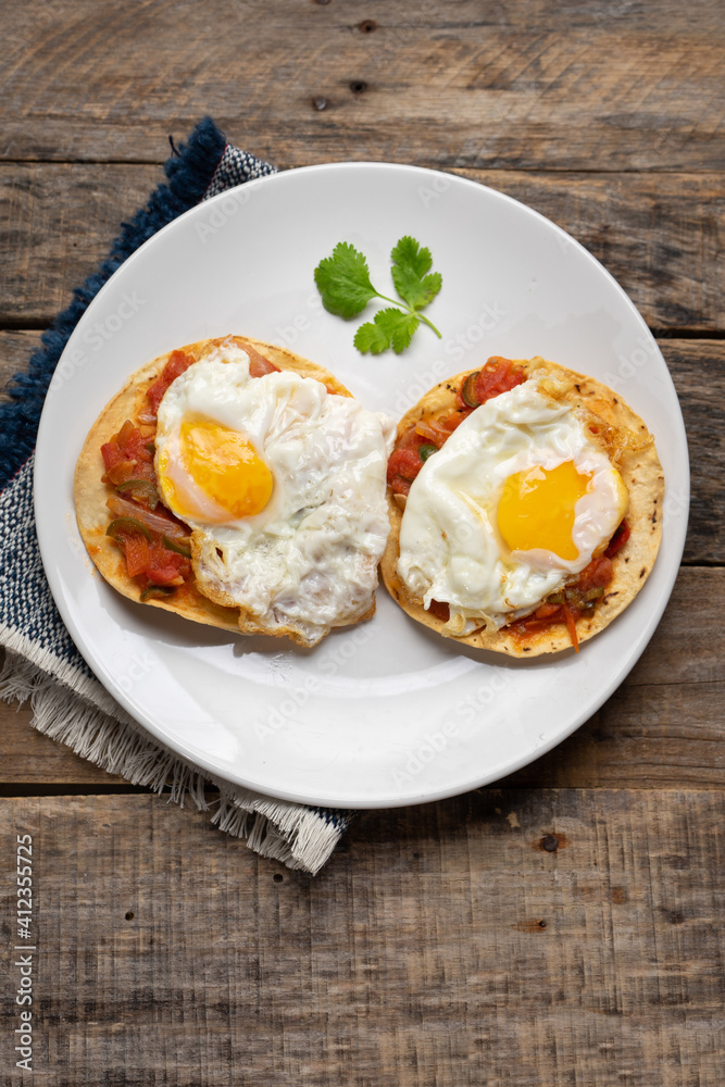 Fried eggs with sauce and tortilla called rancheros for  breakfast on wooden background. Mexican food