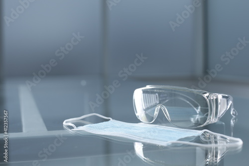 Safety goggles and protective medical mask on glass table