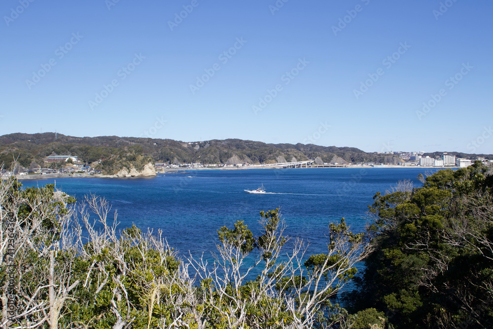 Katsuura Bay in Chiba Japan view, the ocean is a stunning deep blue color and the day is clear. It is a very idyllic scene. High cliffs and green hills.