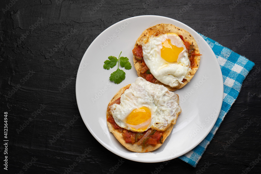 Fried eggs with sauce and tortilla called rancheros for breakfast on dark background. Mexican food Fried eggs with sauce and tortilla called rancheros for breakfast on dark background. Mexican food