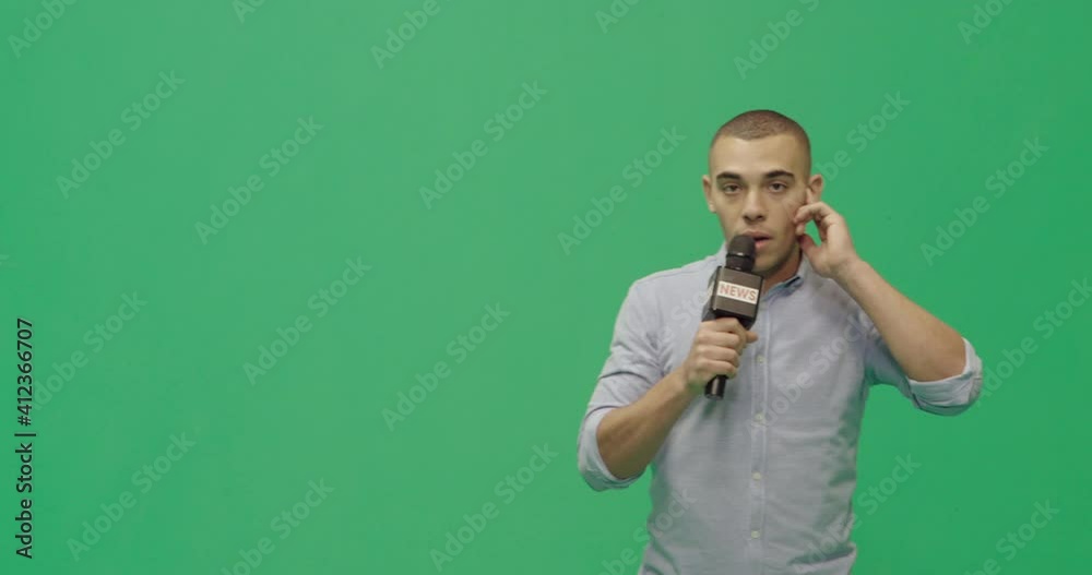 Studio, slow motion, green screen, young male reporter listens to his earpiece, London, UK Studio, slow motion, green screen, young male reporter listens to his earpiece, London, UK
