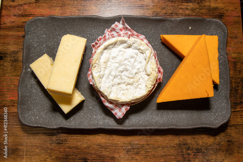 A slate trey of three different types of cheese's on a wooden background