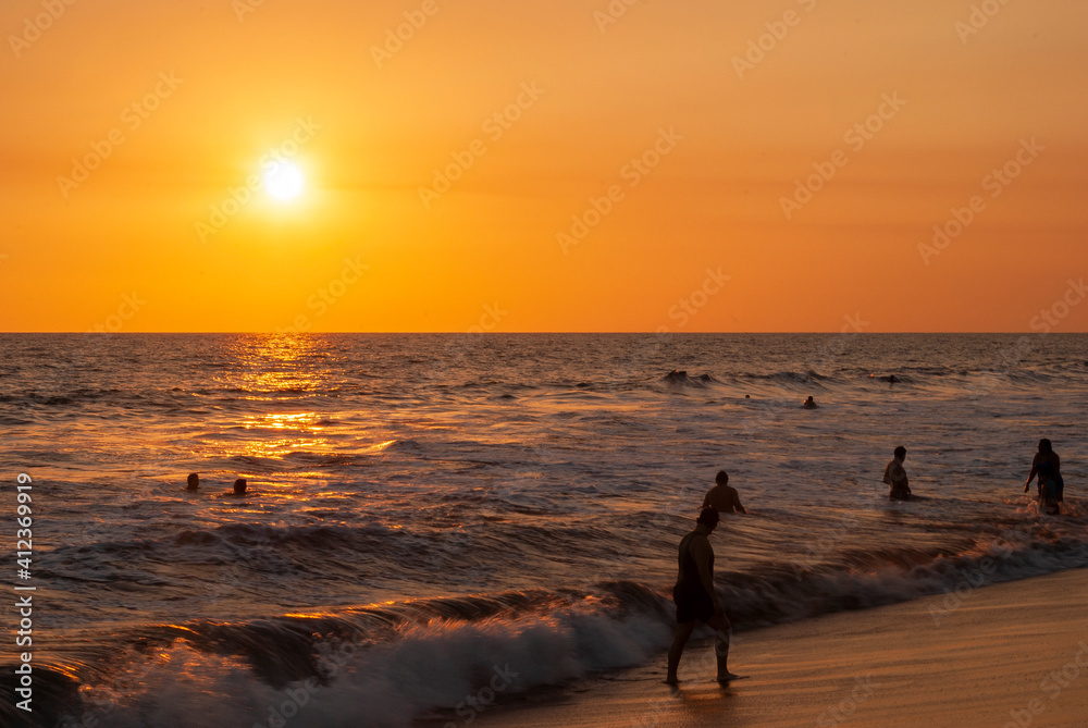 Silhouettes of people bathing on the public beach of Monterrico in Guatemala in the middle of the Covid-19 pandemic, sunset.