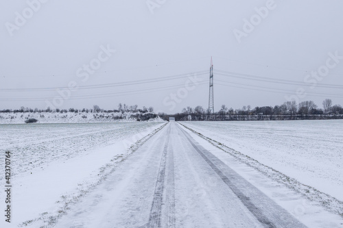 Outdoor scenery diminishing perspective view on street along land and field covered with thick layer snow and background of cloudy overcast sky in countryside in Germany during winter season. © Peeradontax