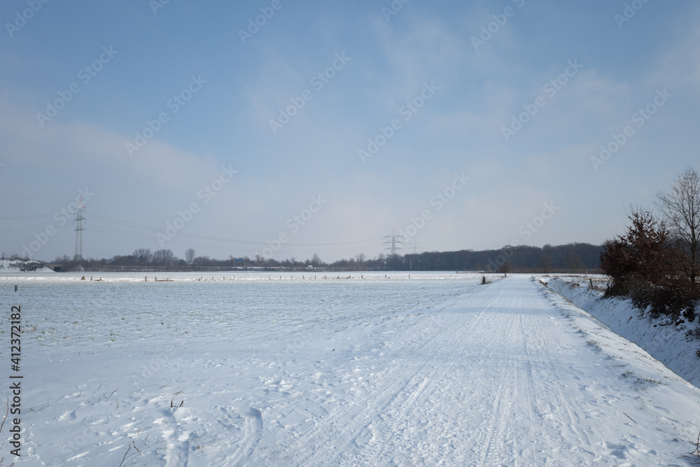 Fototapeta premium Outdoor sunny view of thick layer snow cover street, land and field in countryside in Germany during winter season.