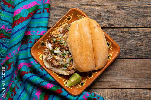 Confit pork sandwich called Torta de carnitas on wooden background. Mexican food photo