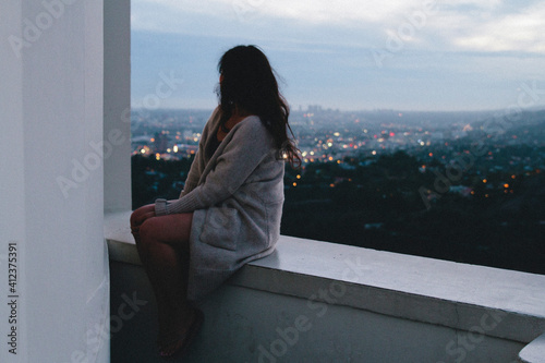 young woman sits on ledge looking out at city skyline photo