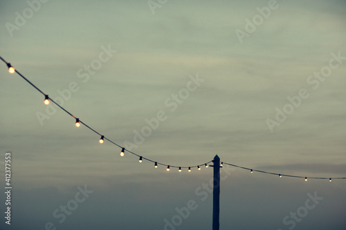 Dusk on a terrace with bulb lights hanging on a pole in Barcelona beach