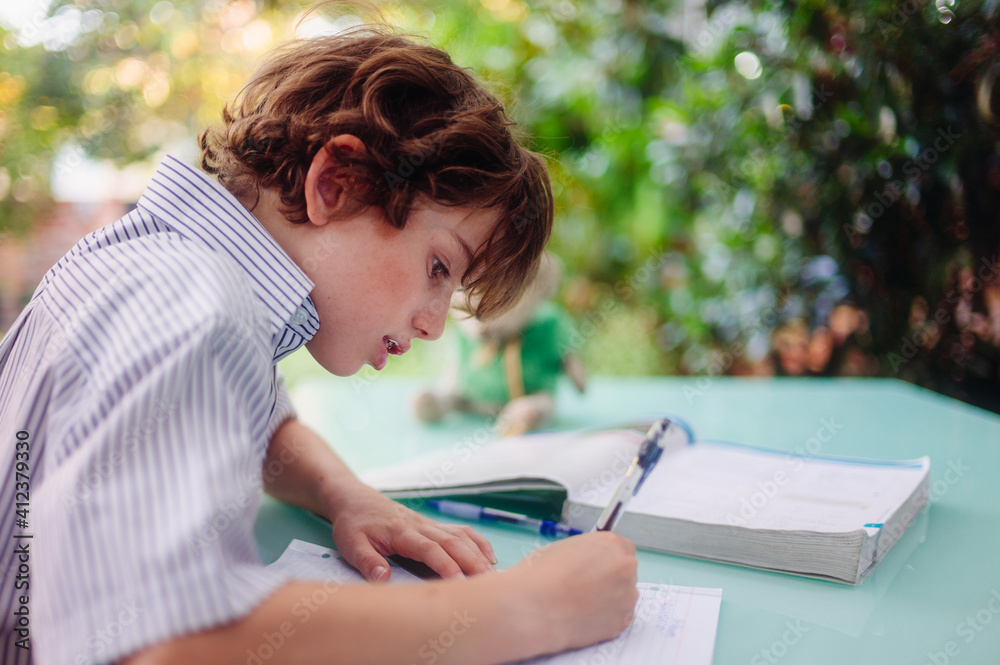 Boy sitting at an outside table doing his homework after school Boy sitting at an outside table doing his homework after school
