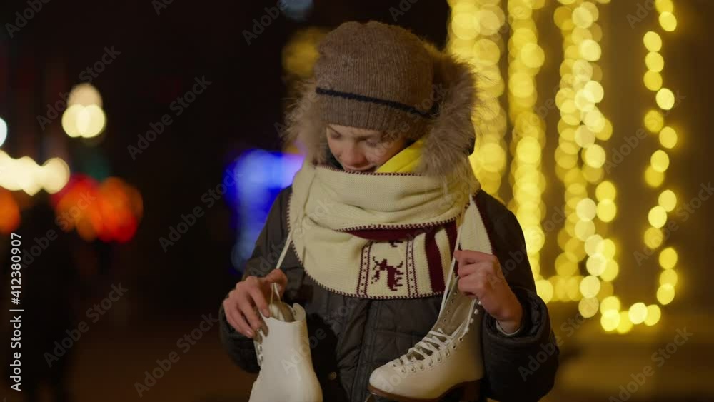 Happy Caucasian boy boasting new ice skates standing on New Year in night city with golden Christmas lights at background. portrait of excited kid bragging holiday gift. Happy Caucasian boy boasting new ice skates standing on New Year in night city with golden Christmas lights at background. portrait of excited kid bragging holiday gift.
