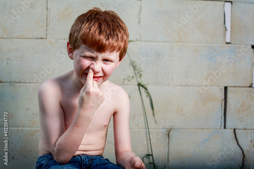 Young redheaded boy picking nose with shirt off photo