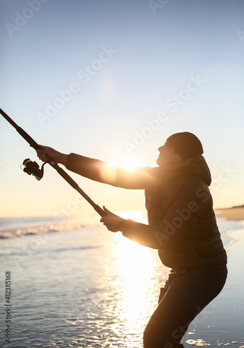 Person casting fishing pole to catch surf fish on atlantic ocean beach photo