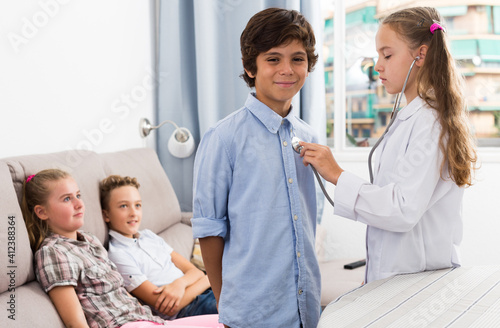 Medic girl with stethoscope with patient boy and children at home