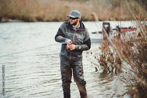 Fly fisherman standing in river fighting a large fish he is hooked up to.