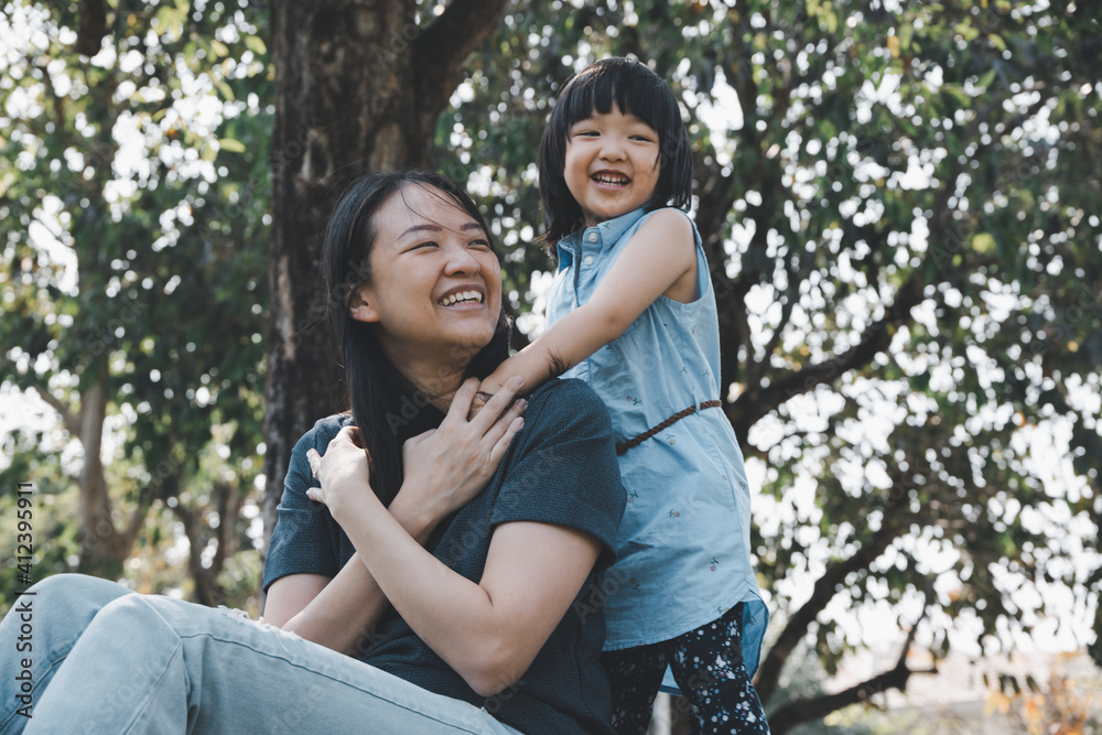 Asian little daughter hug her mom with smile in the park. Concept for family relationship and relaxing time. Asian little daughter hug her mom with smile in the park. Concept for family relationship and relaxing time.