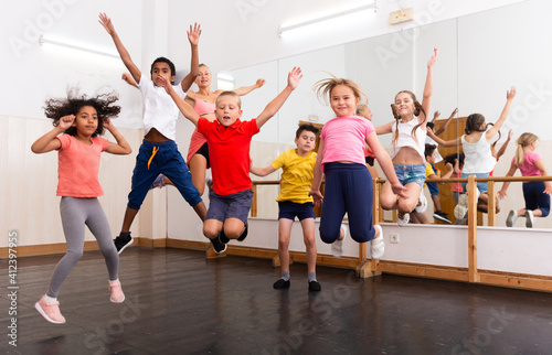 Group of happy sporty kids with female teacher training in modern dance studio, jumping together..
