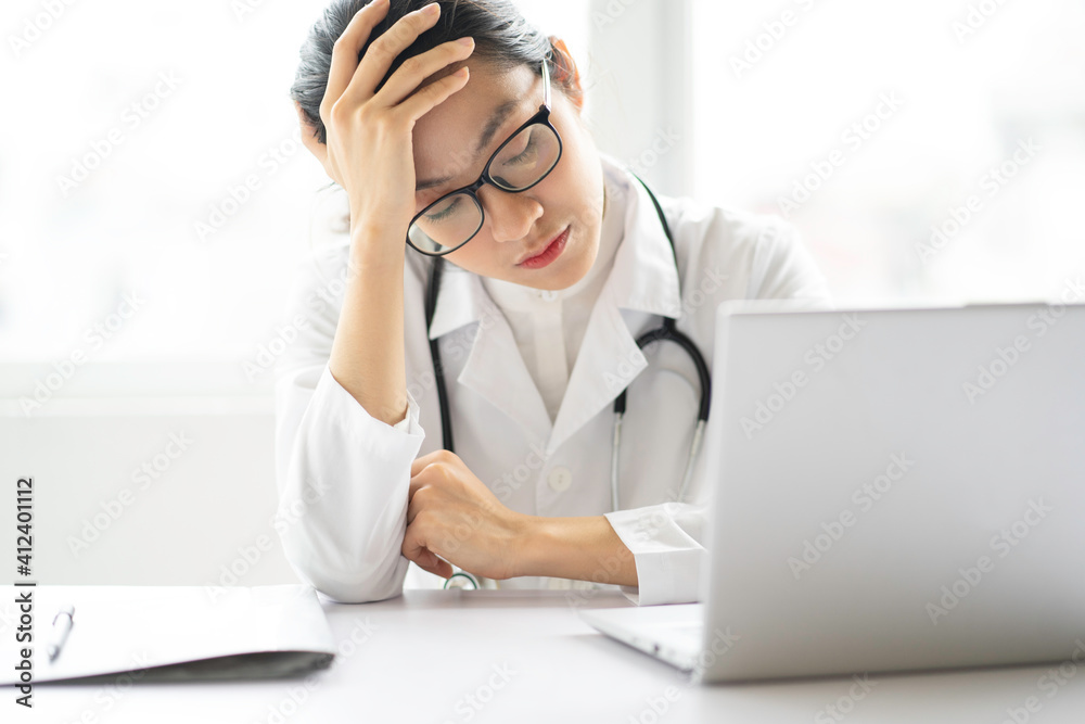 Portrait of young asian female doctor sitting on the desk with tired expression Portrait of young asian female doctor sitting on the desk with tired expression