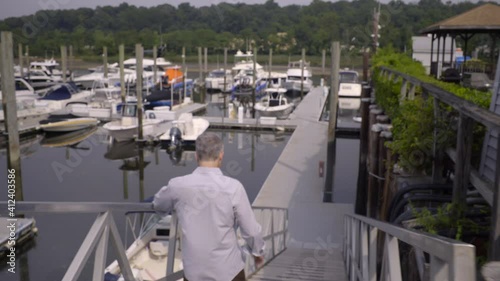 Following Shot of a Man Walking Down Steps and Towards Boats Docked at a Marina photo