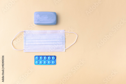Soap, surgical mask and a blister pack of pills on yellow background.
