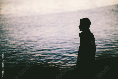 Silhouette of young man with ocean behind him photo