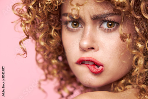 Charming model Close-up curly hair bites her lip pink background bright 