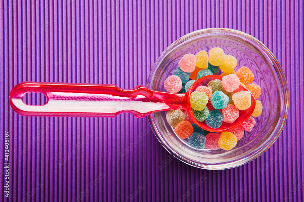 Colourful sugar candy inside a bowl with spoon on green background. Colourful sugar candy inside a bowl with spoon on green background.