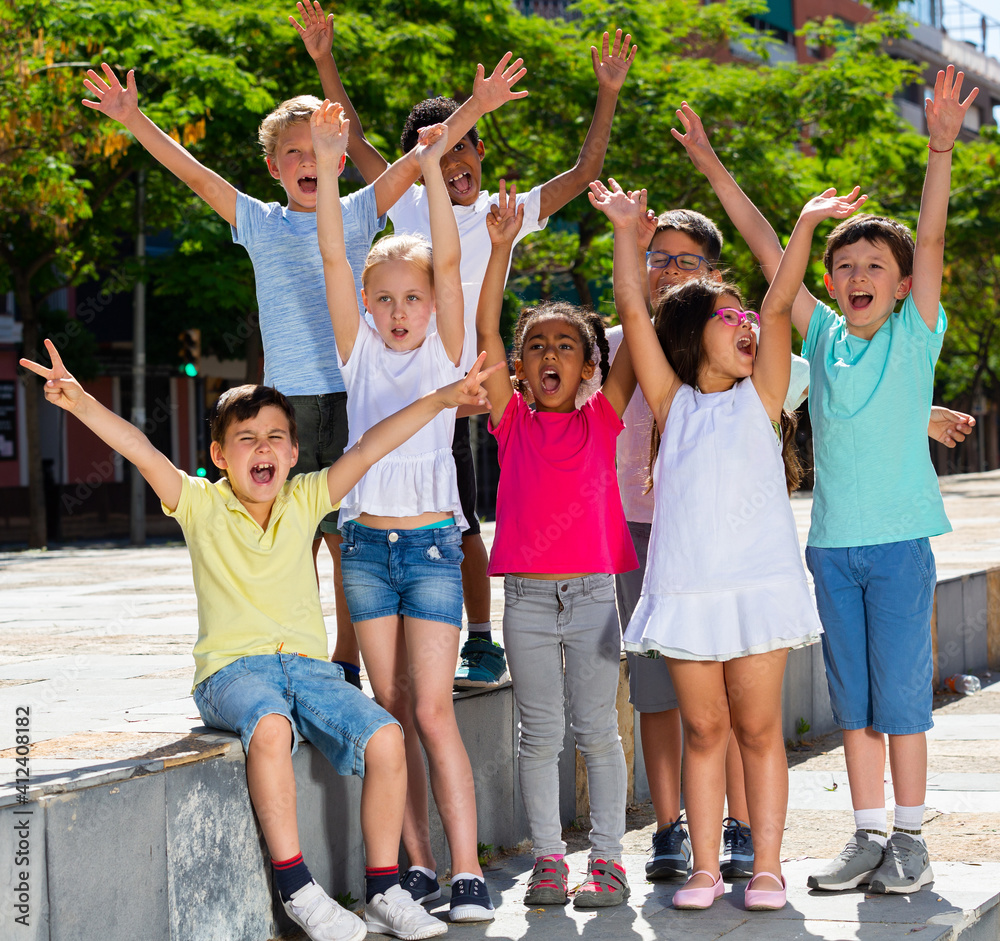 Obraz premium Group of positive children holding hands up and smiling together in park