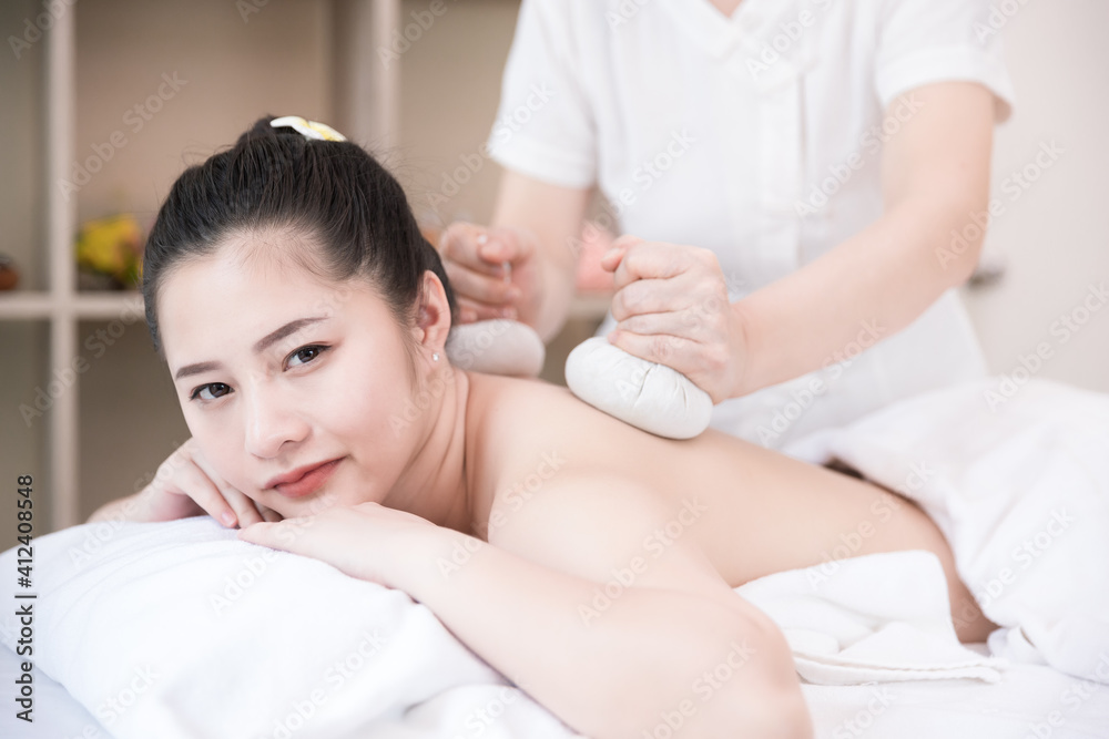 Young Asian woman getting spa massage with Thai Herbal Ball Hot Compress massage at beauty spa salon. Relaxing massage for health