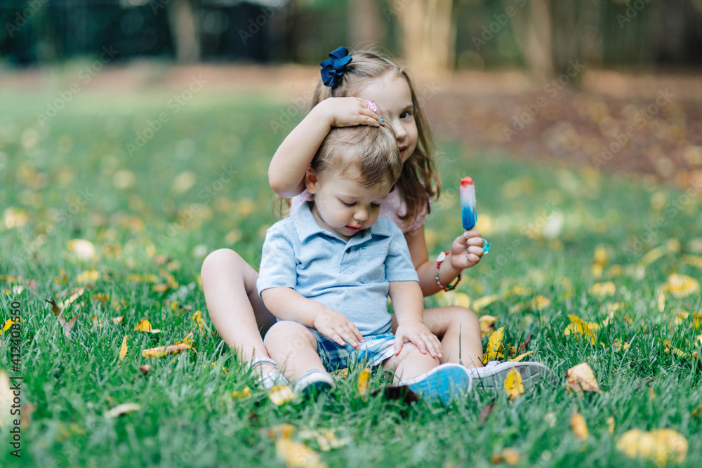 Sister and brother sitting in grass sharing a popsicle Sister and brother sitting in grass sharing a popsicle