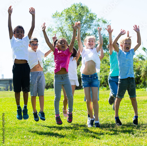 Happy school children jumping on the green lawn. High quality photo