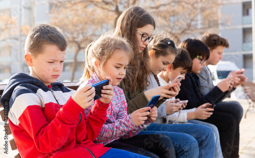 Group of children playing with smartphones outdoors at sunny spring day
