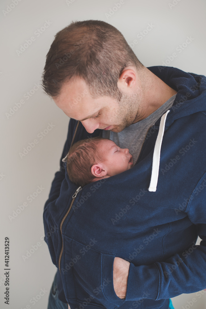 Father carrying his newborn son on his chest covered with a jumper Father carrying his newborn son on his chest covered with a jumper