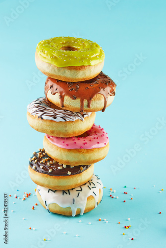 Multicolored donuts with icing and sprinkling stacked in a stack on a blue background