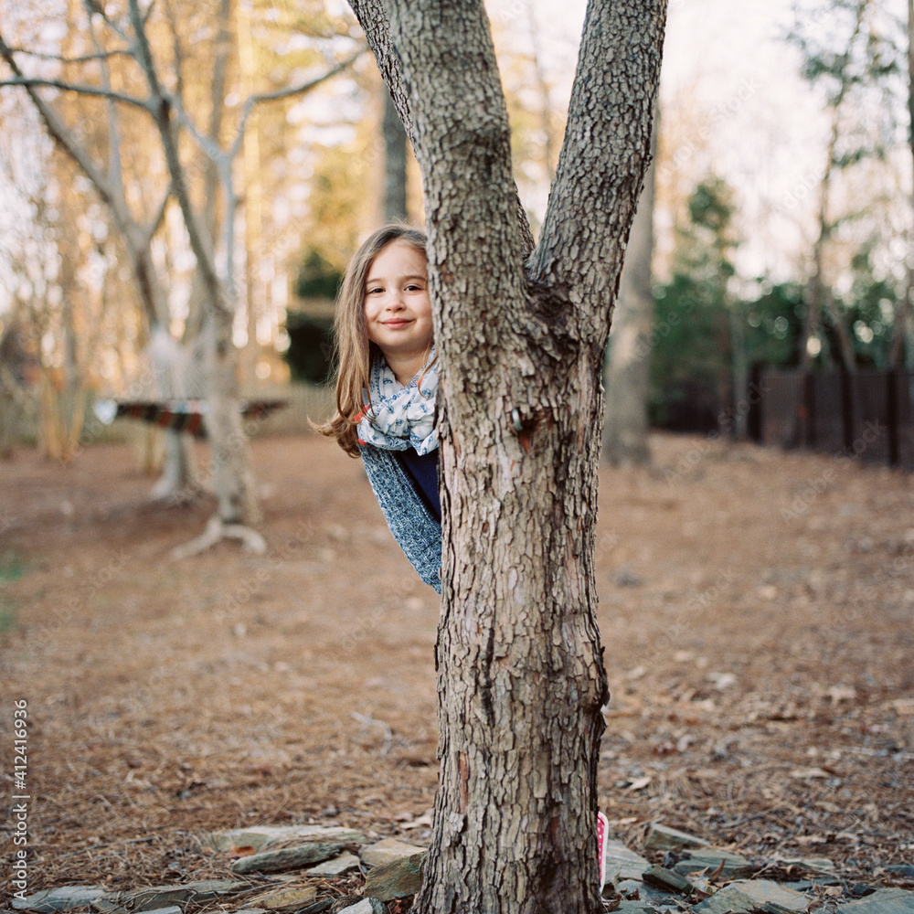 Beautiful young girl peeking out from behind a tree Beautiful young girl peeking out from behind a tree