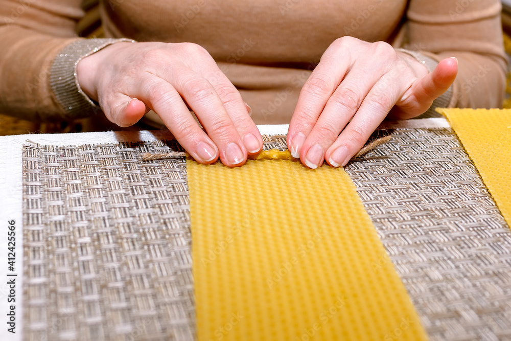 Obraz premium Making a candle from a plate of beeswax. DIY wax candle making process. Step-by-step instruction. Step 3. Twisting. Candle formation.