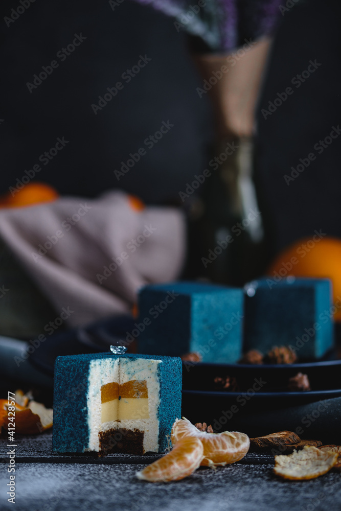 Blue cake filled with orange and tangerine in the shape of a cube. Nearby on a black table are ingredients oranges, tangerines, nuts. Rustic style.
