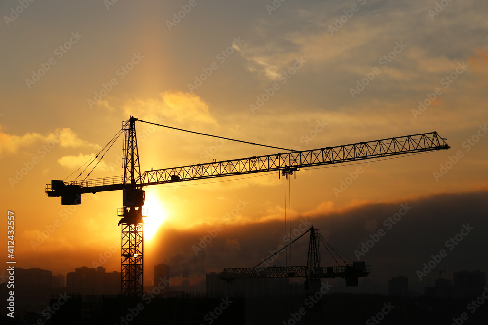 Silhouette of construction crane and unfinished residential building on sunrise background. Housing construction, apartment block in winter city
