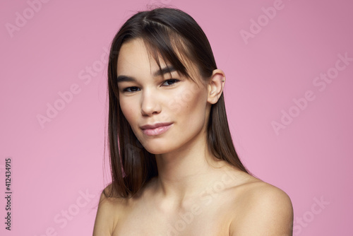 Woman with bare shoulders hair care makeup clean skin pink background