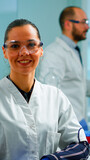 Laboratory doctor looking at camera smiling in modern equipped lab. Multiethnic team examining virus evolution using high tech and chemistry tools for scientific research, vaccine development.