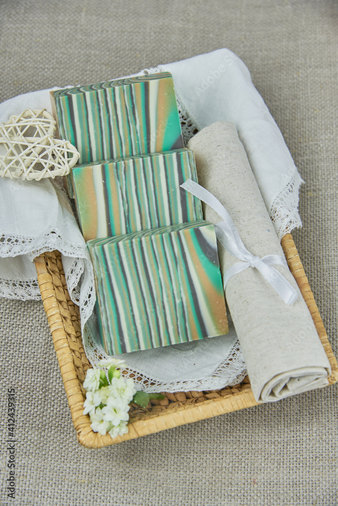 Fototapeta premium Fragrant striped handmade soap in a wicker basket on a white napkin. Personal hygiene items, spa product.