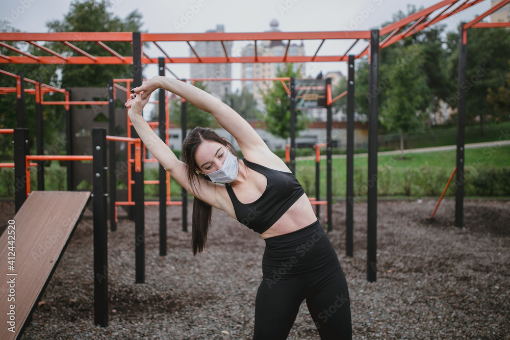 Fototapeta premium A young woman does the sports on the playground wearing a mask coronavirus new normal