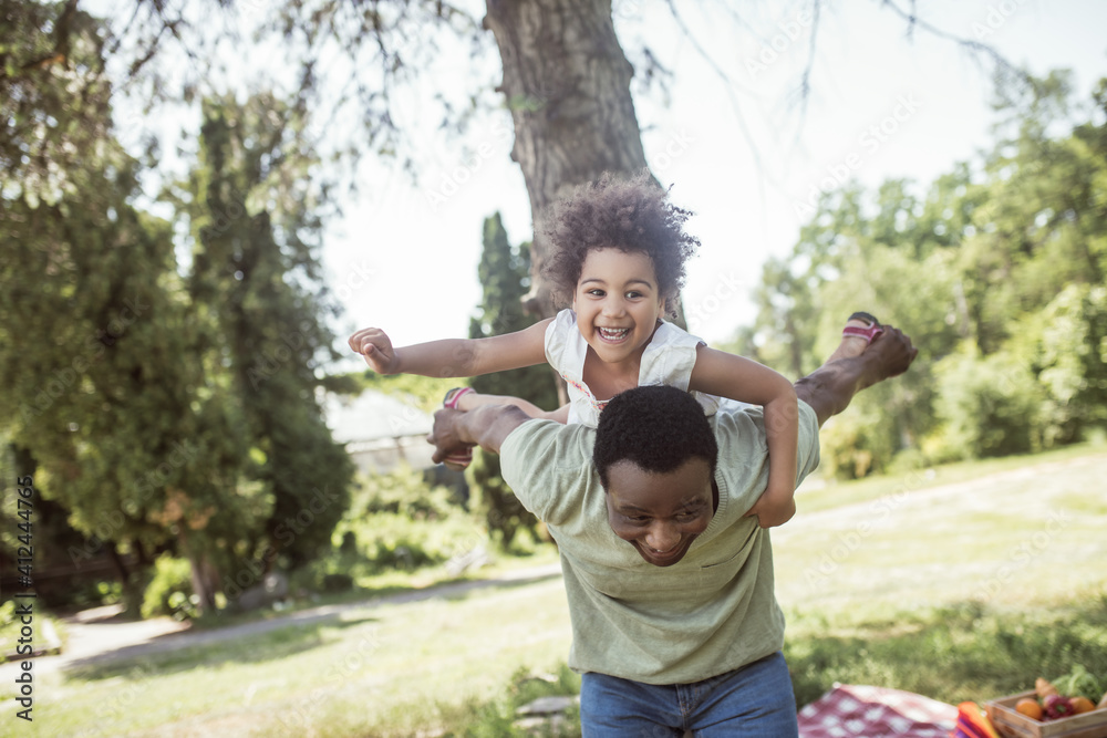 Fototapeta premium African american dad and his daughter having good time together in the park and feeling cheerful