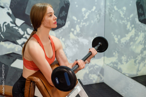 Sporty young beautiful blonde woman holds barbell in gym photo