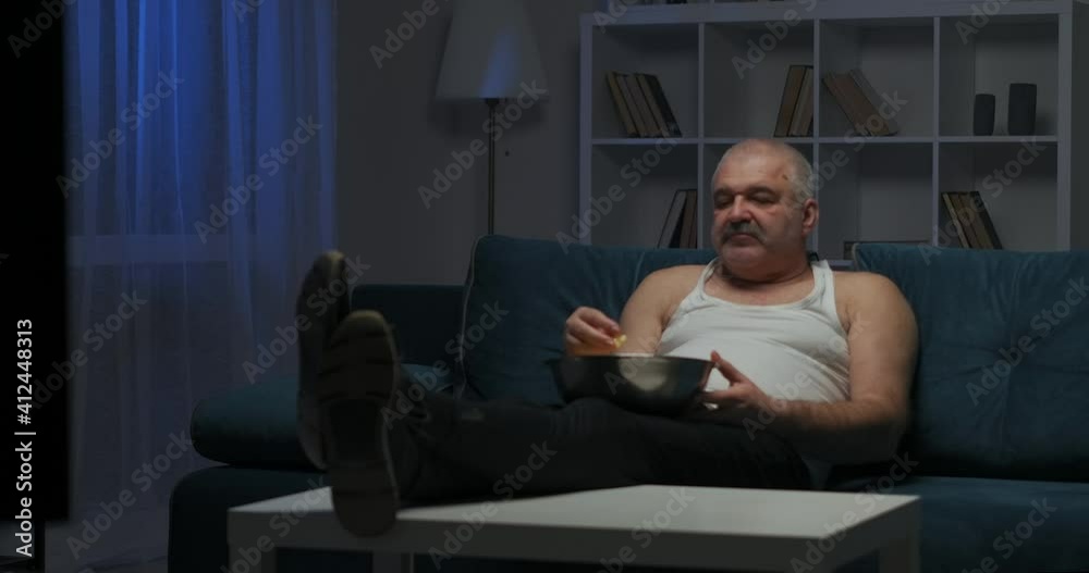 a man with a mustache is watching an action movie on TV and eating popcorn. Bright flash on the screen. a man with a mustache is watching an action movie on TV and eating popcorn. Bright flash on the screen.